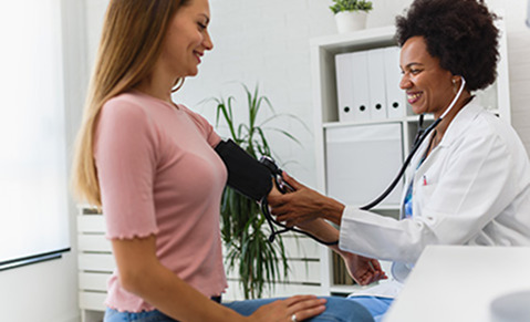 Médecin prend la tension d’une femme, toutes deux souriantes