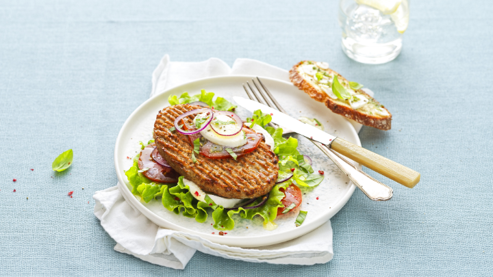 Visuel recette d'un burger végétal estival sur un lit de salade, tomates et burrata