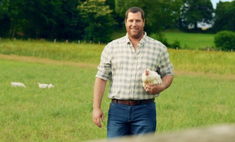 Éleveur de volaille Le Gaulois dans un champs, souriant avec une poule dans les mains