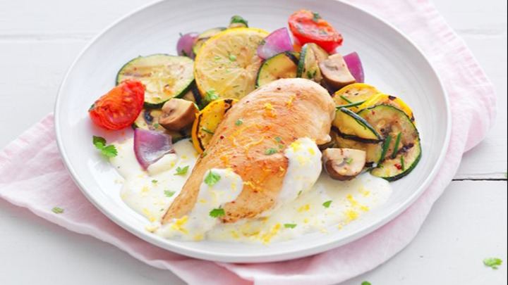 Plat équilibré composé d'un filet de poulet à la crème de citron et de légumes de saison poêlés, disposé dans une assiette blanche et sur un fond rose clair