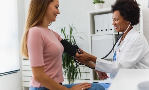 Médecin prend la tension d’une femme, toutes deux souriantes